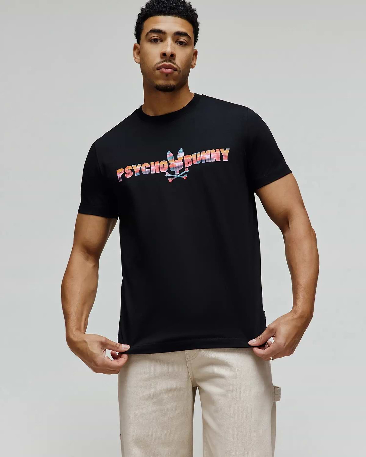 Mens Raphael Wordmark Tee, black classic fit jersey t-shirt featuring a large, vibrant multicolor Psycho Bunny wordmark with an integrated bunny skull graphic on the chest. (1)