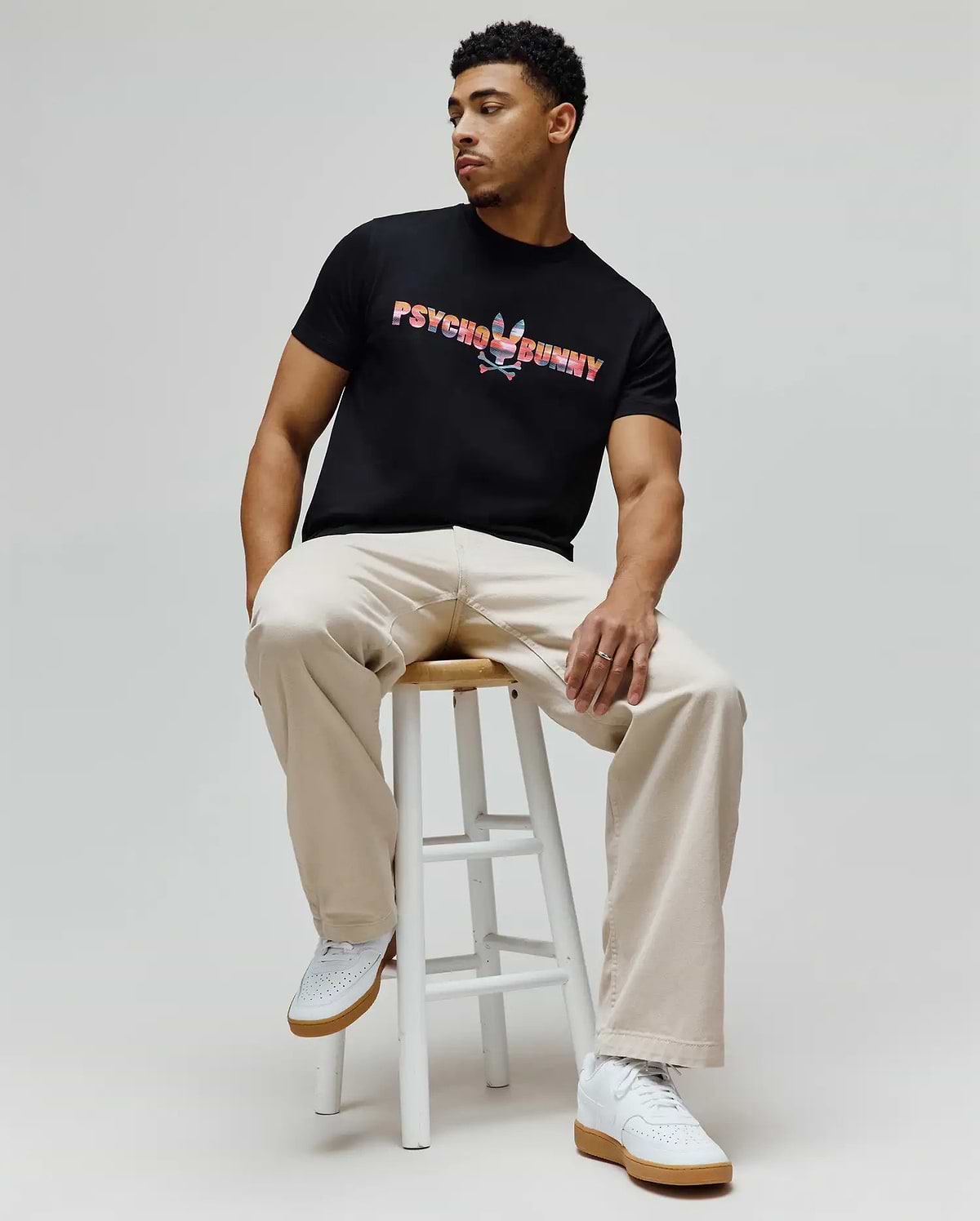 Mens Raphael Wordmark Tee, a classic fit black jersey t-shirt featuring a large, vibrant multi-color striped Psycho Bunny wordmark and skull logo on the chest. (3)