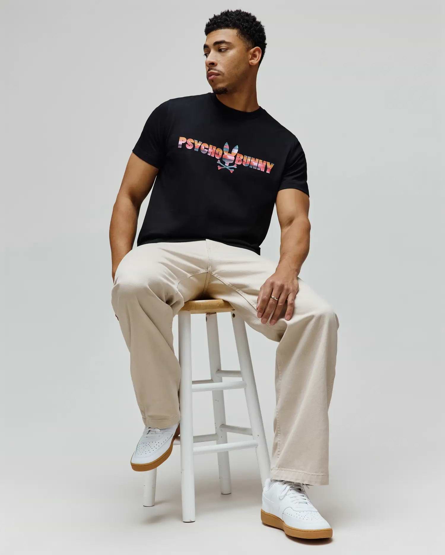 Mens Raphael Wordmark Tee, a classic fit black jersey t-shirt featuring a large, vibrant multi-color striped Psycho Bunny wordmark and skull logo on the chest. (3)