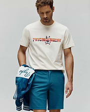 Mens Raphael Wordmark Tee, an off-white jersey tee with a large, colorful striped Psycho Bunny wordmark and bunny skull chest logo. Teal shorts and a satin jacket with embroidered Psycho script. (1)