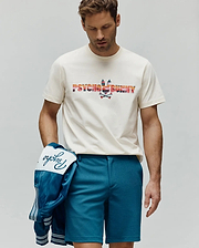 Mens Raphael Wordmark Tee, an off-white jersey tee with a large, colorful striped Psycho Bunny wordmark and bunny skull chest logo. Teal shorts and a satin jacket with embroidered Psycho script. (1)