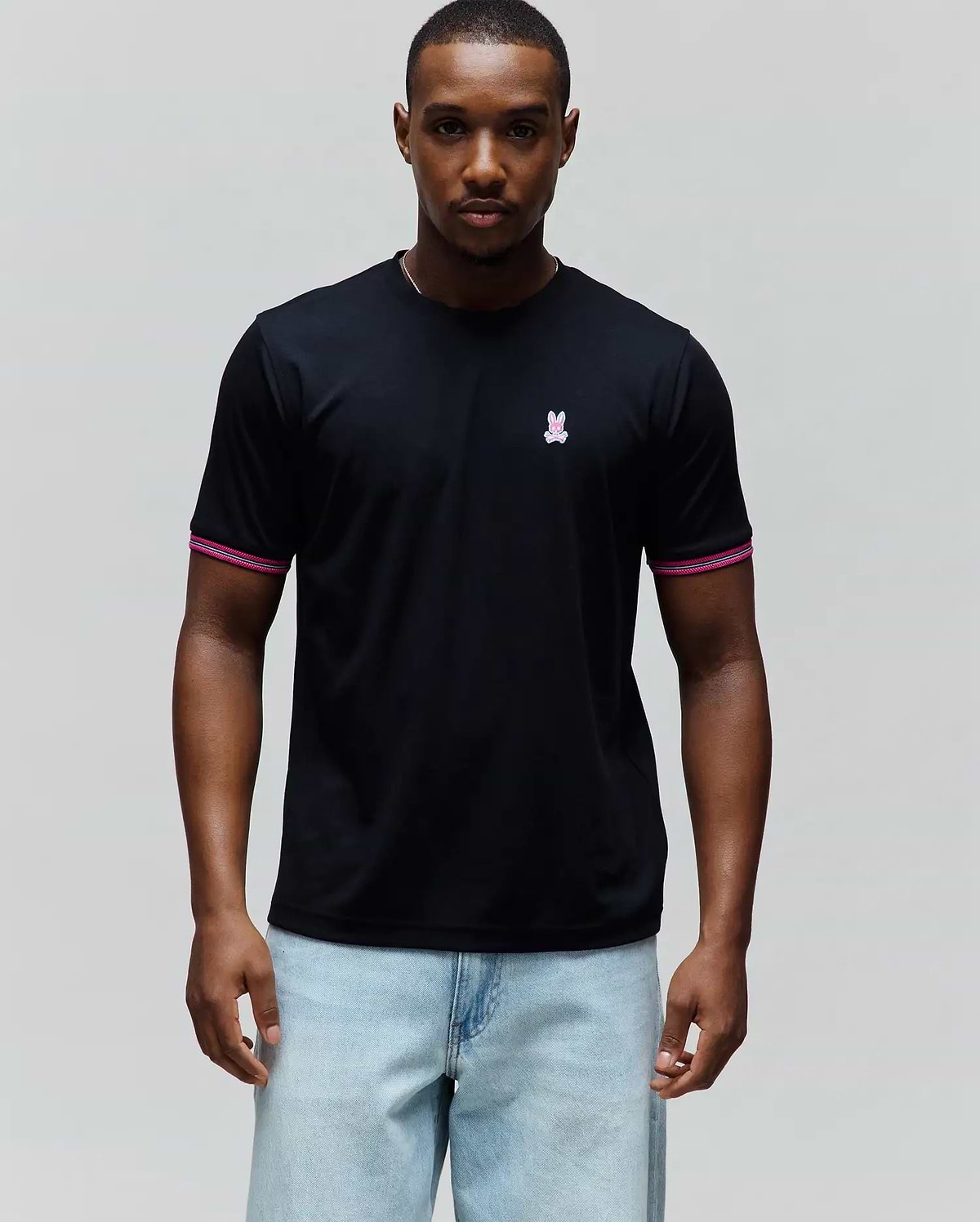 Mens Clark Performance Tee, a black classic fit smooth jersey t-shirt with a small embroidered pink and white Psycho Bunny skull logo on the left chest and ribbed sleeve cuffs featuring pink and white stripes.