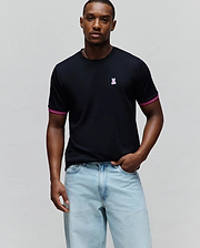 Mens Clark Performance Tee, black jersey knit with a classic fit, featuring a small embroidered pink and white Psycho Bunny skull logo on the left chest and striped pink and white cuffs.