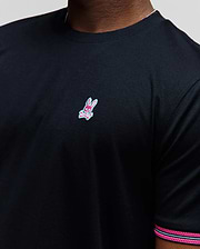 Mens Clark Performance Tee, black classic fit smooth jersey knit with a small embroidered pink and light blue Psycho Bunny skull logo on the left chest and striped sleeve trim.