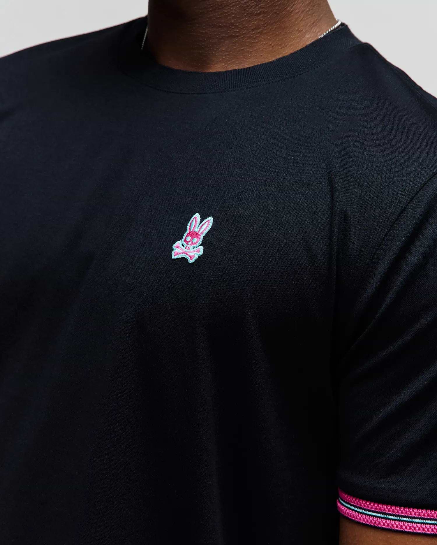 Mens Clark Performance Tee, black classic fit smooth jersey knit with a small embroidered pink and light blue Psycho Bunny skull logo on the left chest and striped sleeve trim.