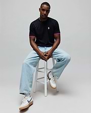 Mens Clark Performance Tee, a black classic fit jersey t-shirt with a small embroidered pink Psycho Bunny skull logo on the left chest and pink striped sleeve cuffs.