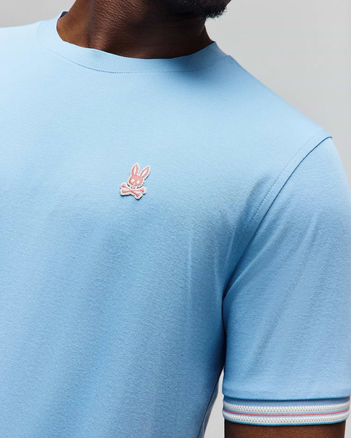Mens Clark Performance Tee, a light blue classic fit jersey knit t-shirt with a small embroidered pink Psycho Bunny skull logo on the left chest and a striped sleeve cuff. (2)