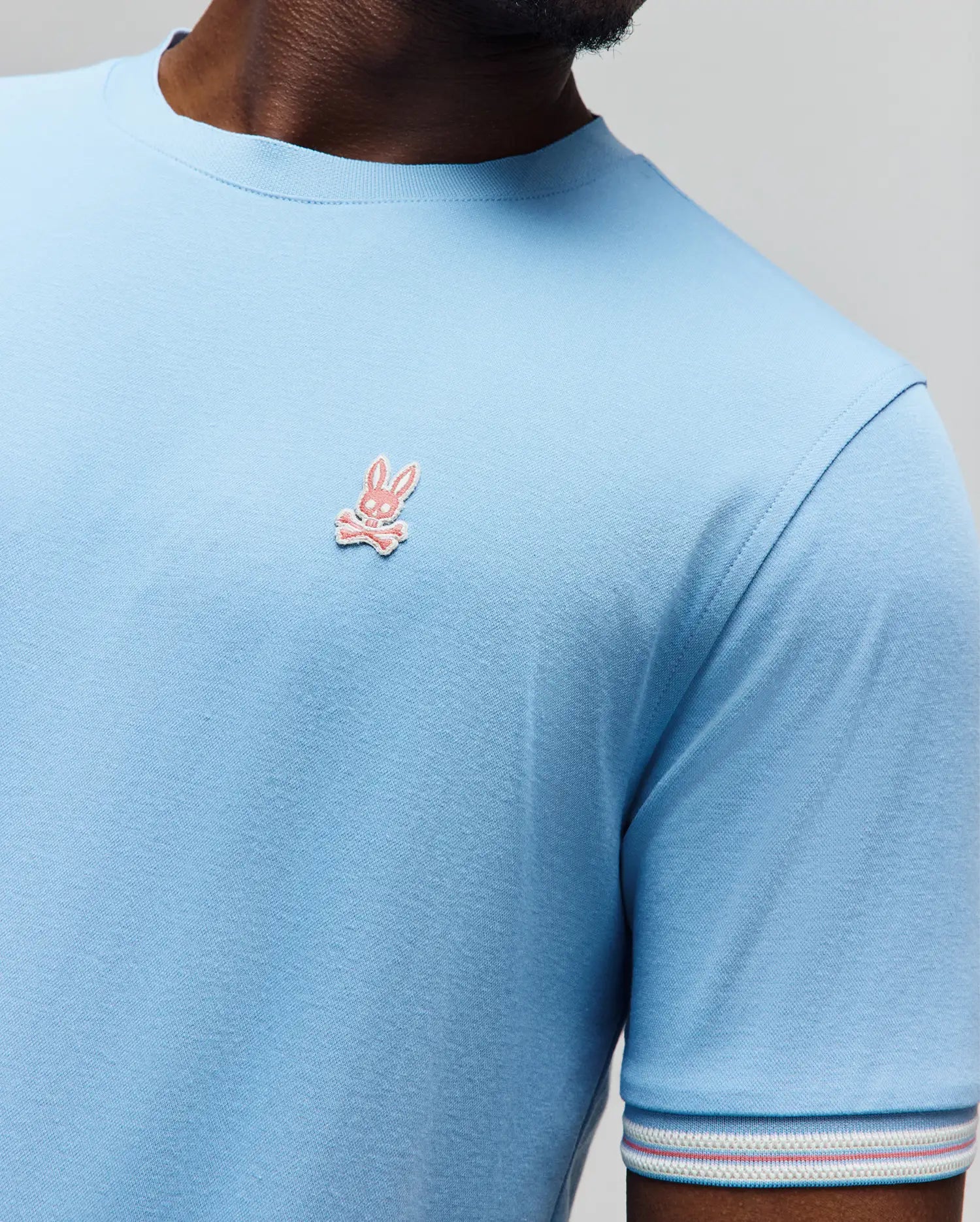 Mens Clark Performance Tee, a light blue classic fit jersey knit t-shirt with a small embroidered pink Psycho Bunny skull logo on the left chest and a striped sleeve cuff. (2)