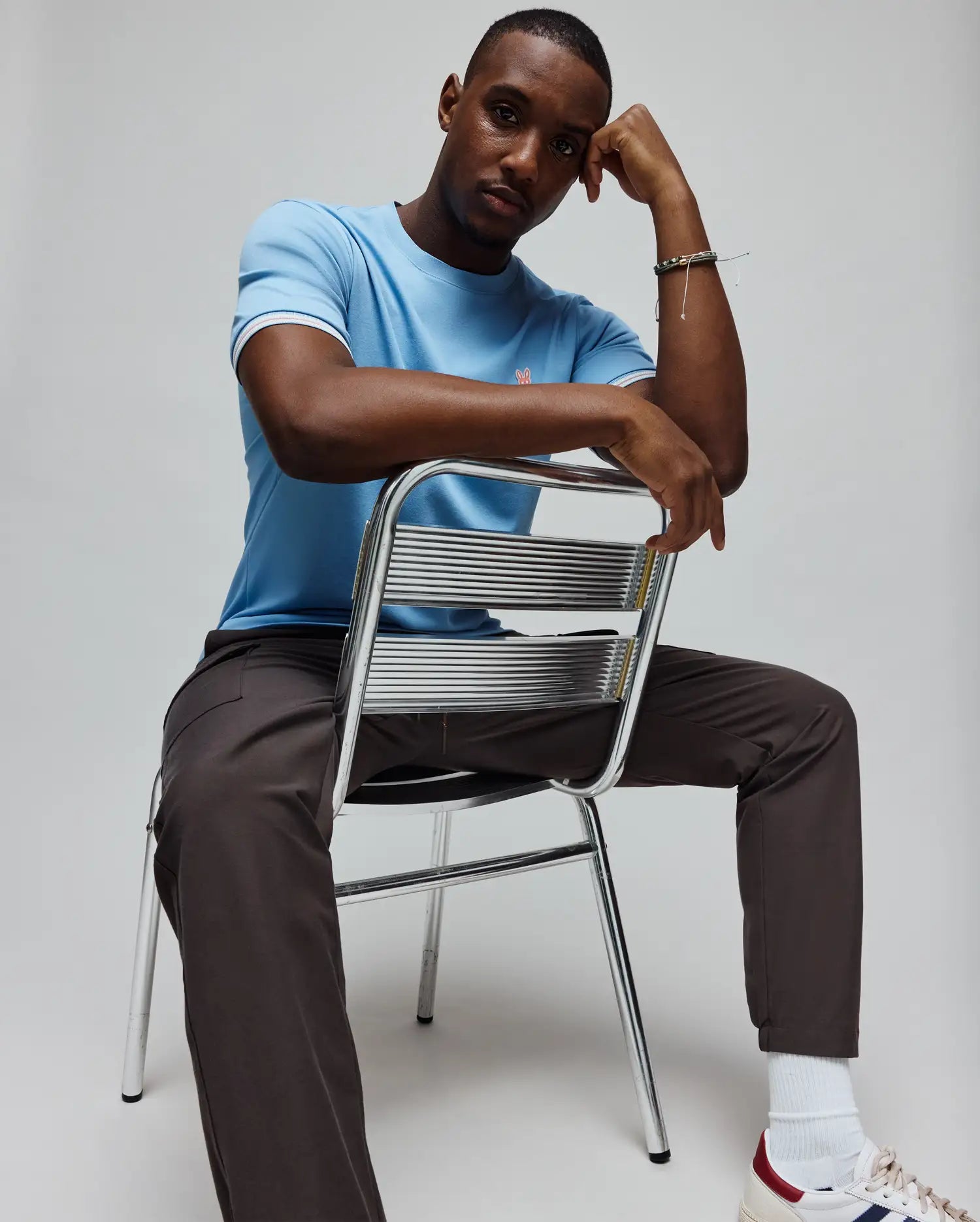 Mens Clark Performance Tee, a light blue classic fit jersey knit t-shirt with a small pink embroidered Psycho Bunny skull logo on the left chest and white, red, navy striped sleeve cuffs. (3)
