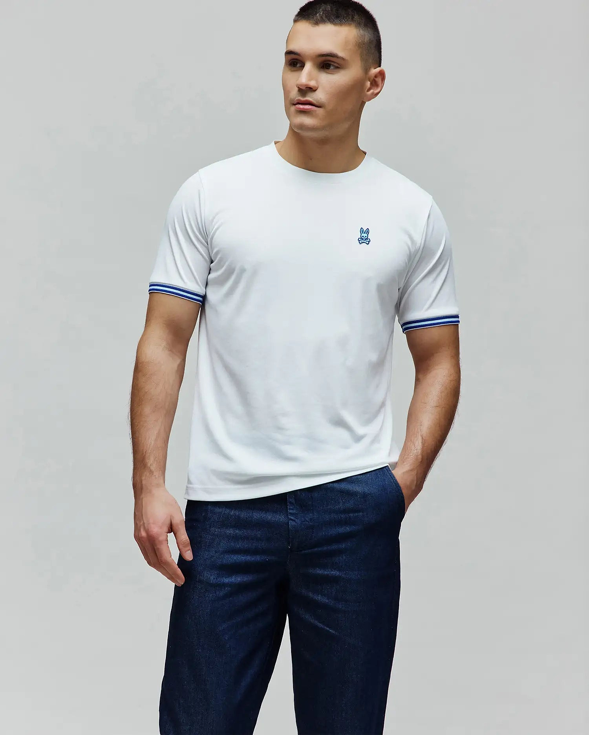 White Mens Clark Performance Tee, a classic fit performance jersey with a small blue embroidered Psycho Bunny skull logo on the left chest and blue and white striped ribbed cuffs. (3)