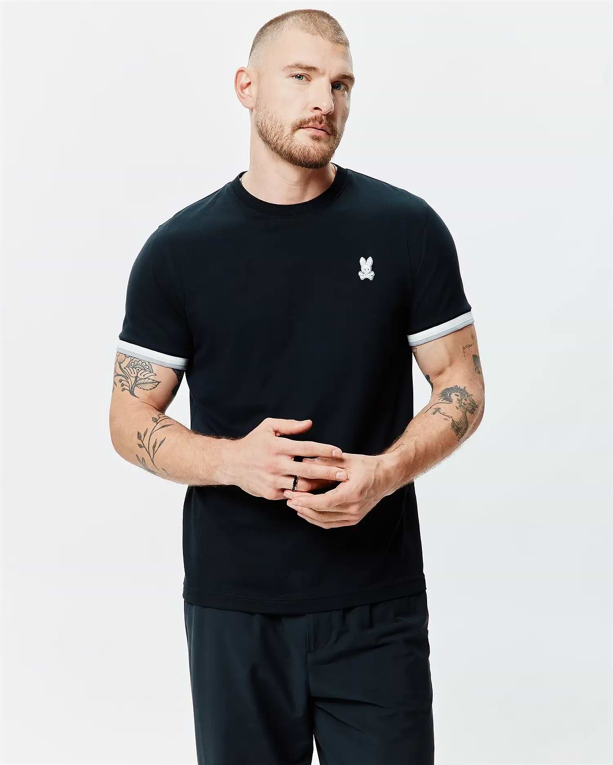 Mens Holden Tee, a classic fit black jersey knit t-shirt with a ribbed crew neck, white striped sleeve cuffs, and a small embroidered white Psycho Bunny skull logo on the left chest.