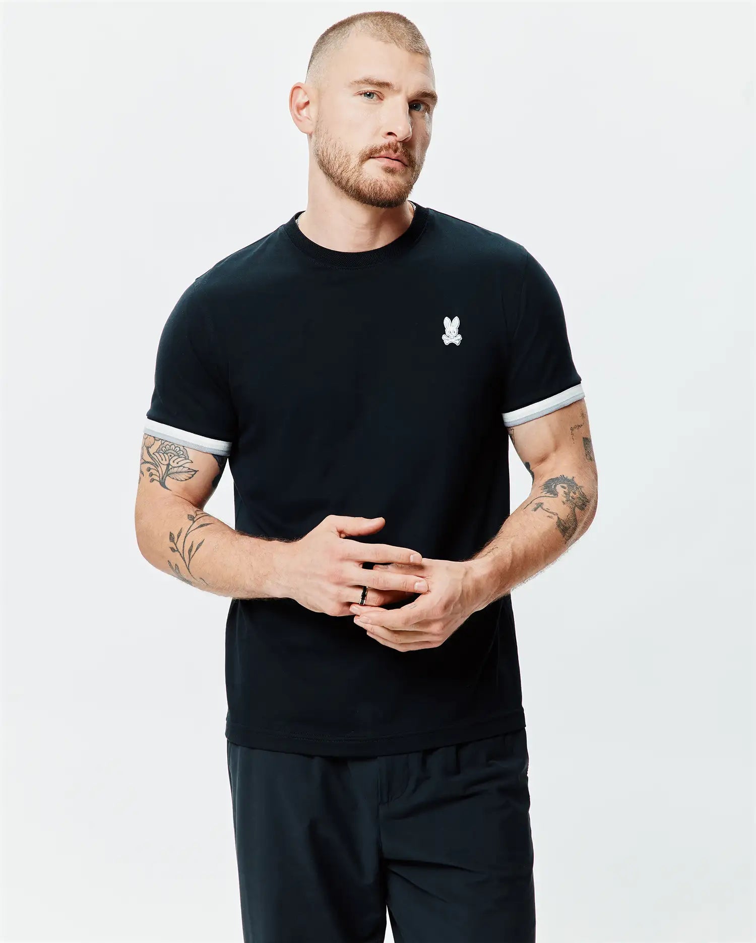 Mens Holden Tee, a classic fit black jersey knit t-shirt with a ribbed crew neck, white striped sleeve cuffs, and a small embroidered white Psycho Bunny skull logo on the left chest.