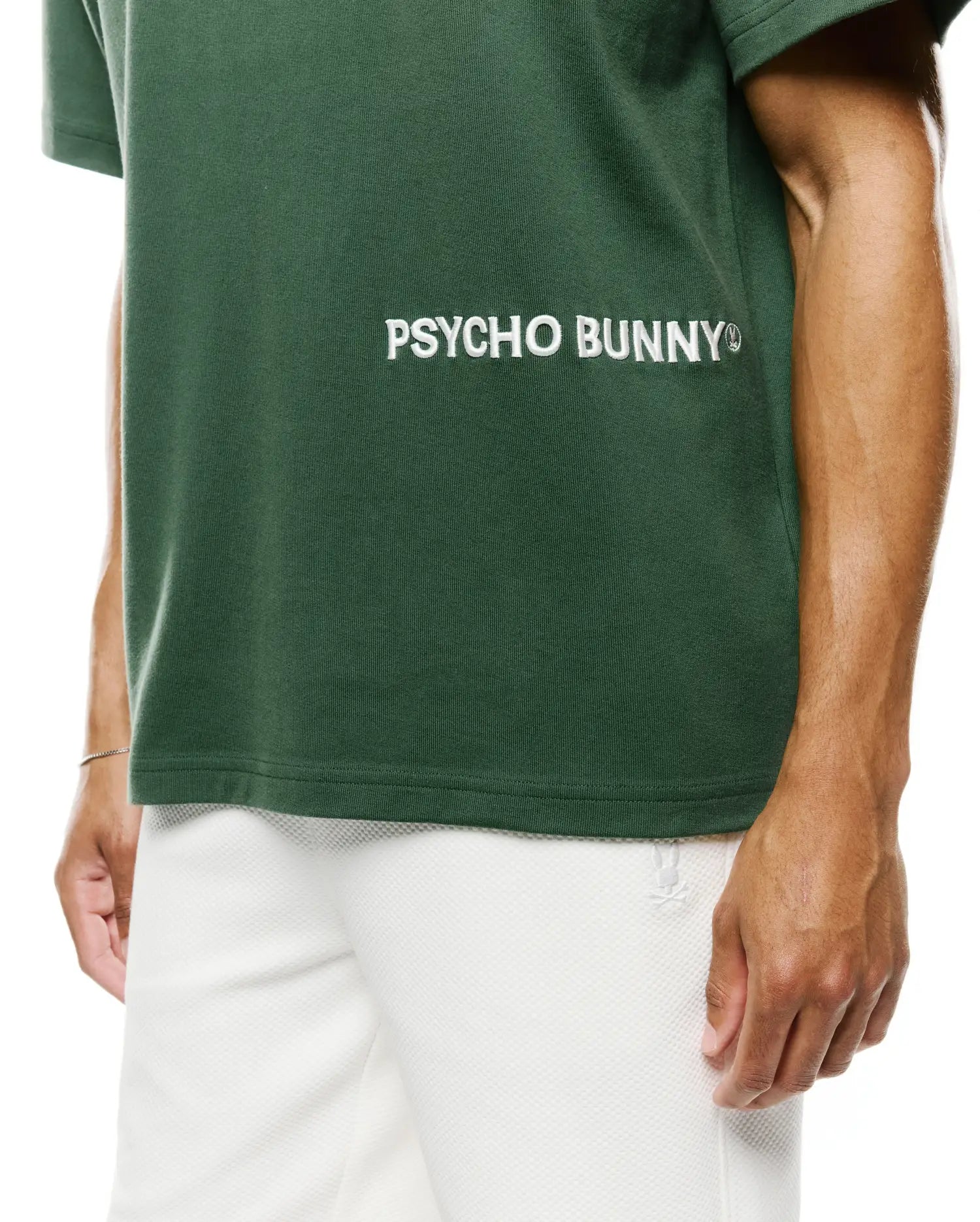 Mens Haiden Relaxed Heavy Weight Tee in dark green heavyweight jersey, featuring a large white embroidered Psycho Bunny text logo on the chest, paired with white textured shorts displaying a small bunny skull logo.