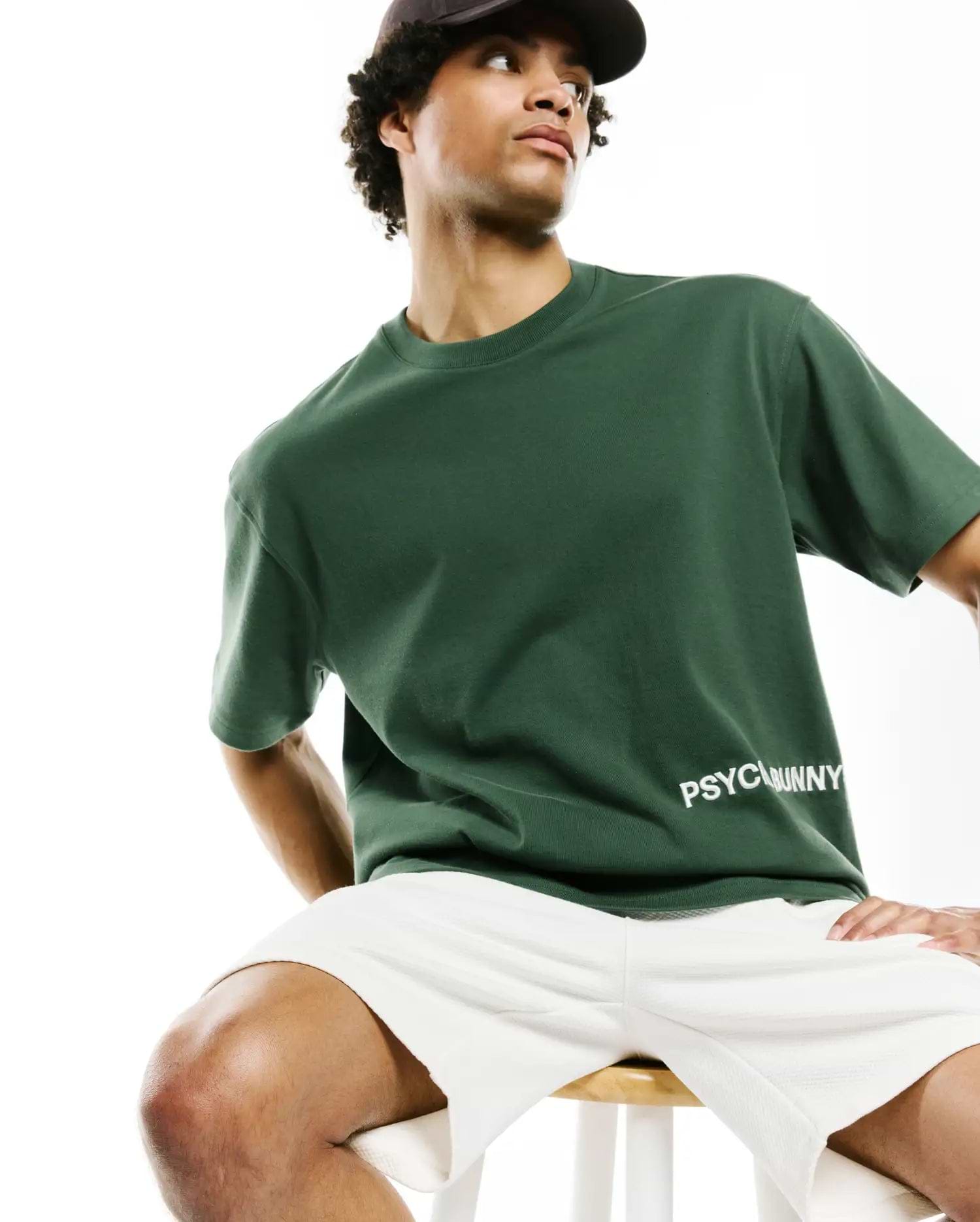 Mens Haiden Relaxed Heavy Weight Tee, a premium dark green jersey with a smooth texture, featuring the iconic white PSYCHOBUNNY text logo on the lower front.