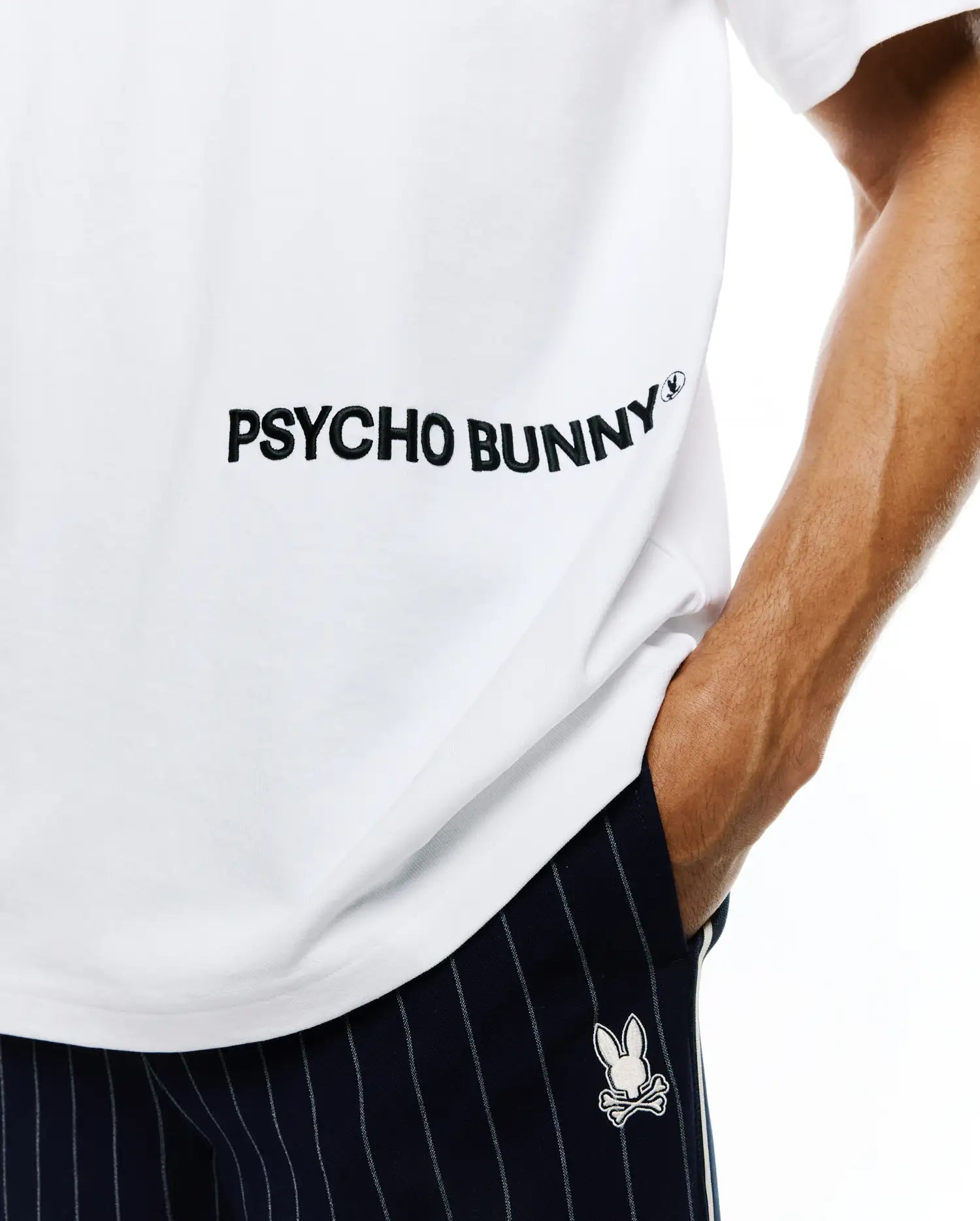 Mens Haiden Relaxed Heavy Weight Tee in white jersey with large black PSYCHO BUNNY text and small bunny skull logo, paired with navy pinstripe shorts featuring an embroidered white bunny skull.