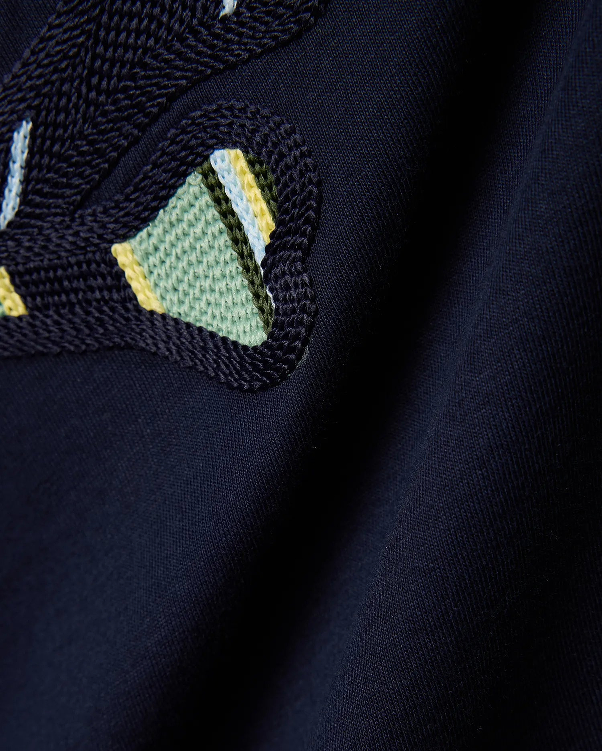 Mens Drew Embroidered Graphic Tee, a dark navy jersey knit with a prominent, textured Psycho Bunny skull logo detail featuring light blue, yellow, and green stripes.