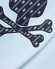 Mens Jaden Graphic Tee in light blue jersey knit, featuring a large navy blue skull and crossbones graphic with white Psycho Bunny logo and checkered stripe pattern, outlined in black embroidery.