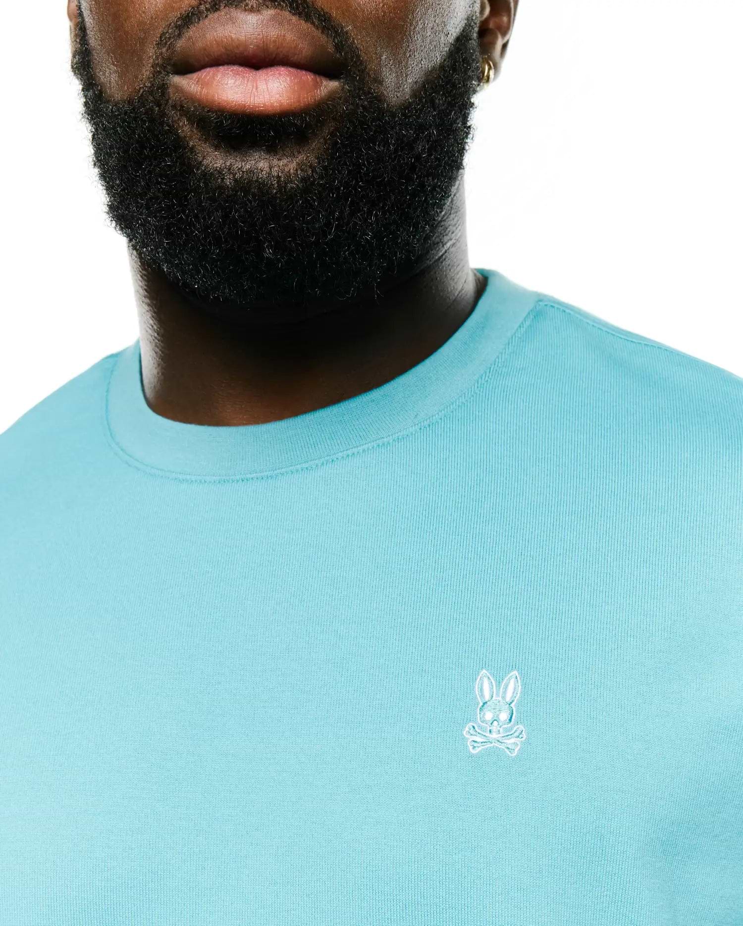 Men's Norman Longsleeve Oversized Tee in aqua blue, featuring a soft jersey knit fabric, ribbed crewneck, and a small white embroidered Psycho Bunny skull logo on the left chest. (2)