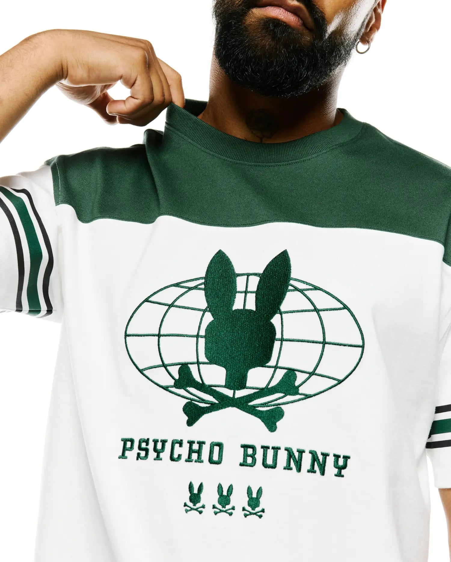 Mens Mike Graphic Jersey Tee, white with green color block. Features an embroidered green Psycho Bunny skull globe graphic, PSYCHO BUNNY text, and three bunny logos on the chest, with striped sleeves. (3)