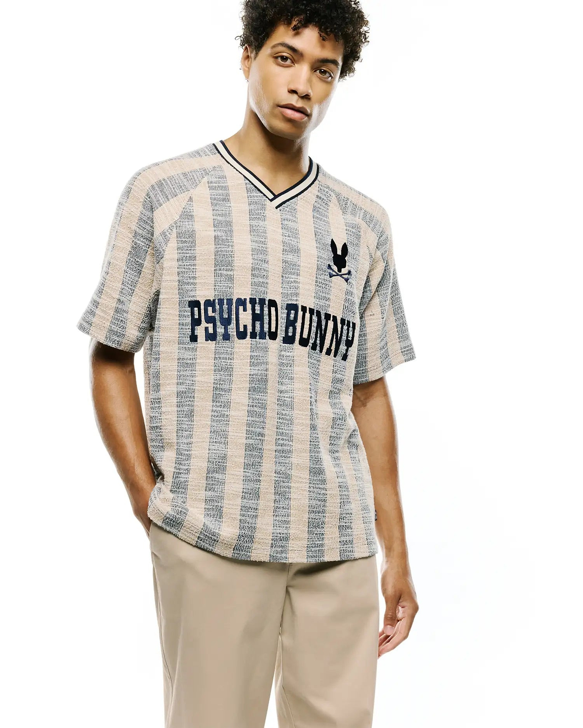 Mens Nathaniel Relaxed Raglan Tee in beige and blue vertical stripe textured knit, featuring a navy V-neck, embroidered Psycho Bunny skull logo, and large PSYCHO BUNNY text across the chest.