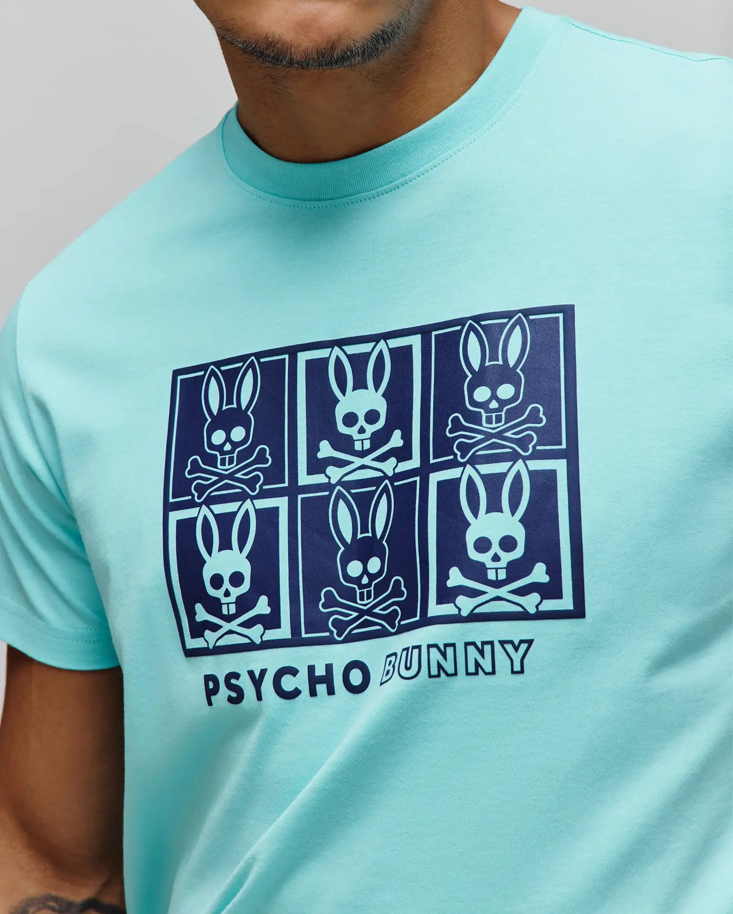 Mens Keon Graphic Tee in aqua, featuring a classic fit and smooth jersey knit. A large navy chest graphic displays six Psycho Bunny skull logos in a grid with PSYCHO BUNNY text.