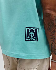 Mens Keon Graphic Tee, aqua smooth jersey knit, classic fit, with a dark blue Psycho Bunny skull and crossbones graphic in a square frame on the lower left side.