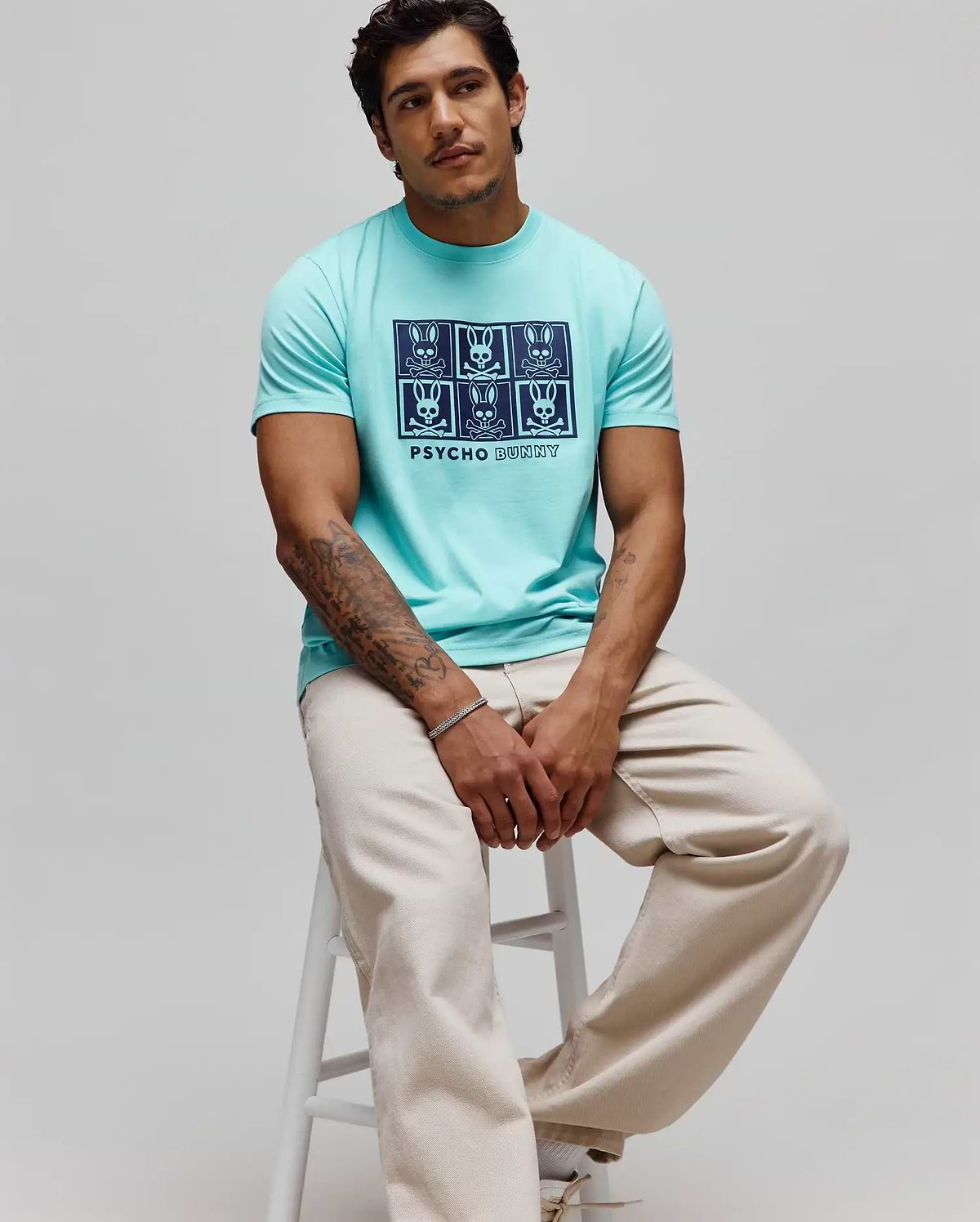 Mens Keon Graphic Tee, an aqua classic fit smooth jersey t-shirt with a large dark blue chest graphic featuring a 2x3 grid of Psycho Bunny skull logos and PSYCHO BUNNY text.