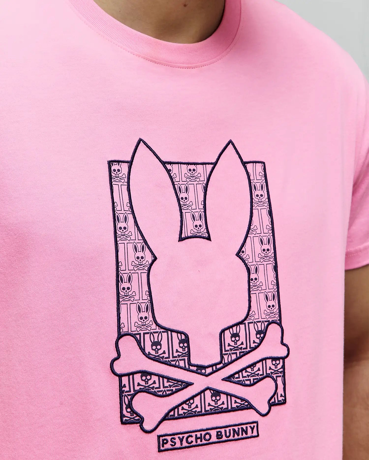 Mens Keon Embroidered Graphic Tee: Classic fit pink jersey t-shirt with a large central dark blue embroidered Psycho Bunny skull graphic, featuring a repeating bunny skull and crossbones pattern inside, and Psycho Bunny text below. (3)