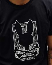 Black classic fit jersey Mens Keon Embroidered Graphic Tee with a large central white embroidered Psycho Bunny skull graphic, featuring a repeating bunny skull and crossbones pattern and PSYCHO BUNNY text. (2)