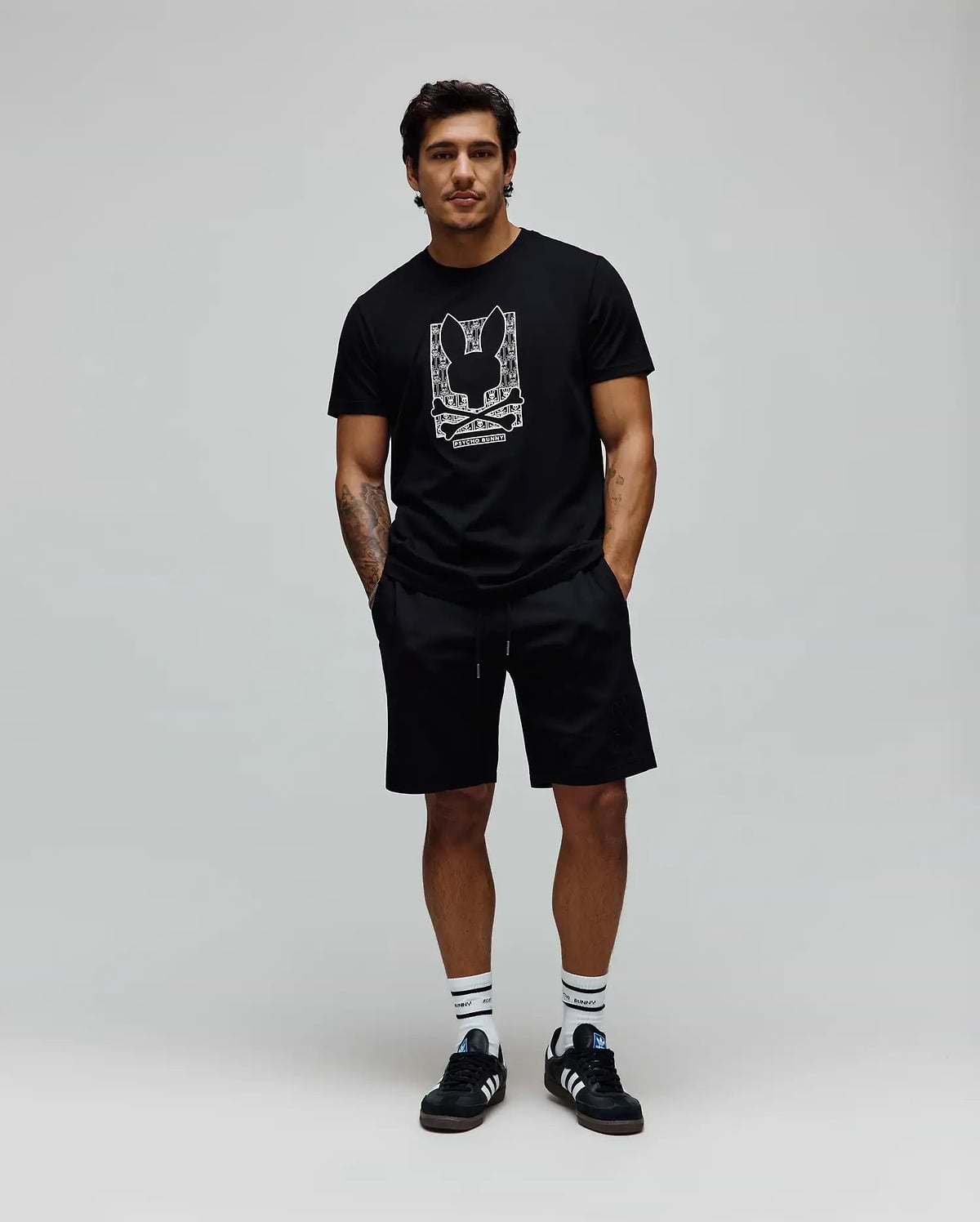 Mens Keon Embroidered Graphic Tee. Black classic-fit jersey t-shirt with a large white embroidered Psycho Bunny skull logo graphic and text on the chest, complemented by black relaxed shorts. (3)