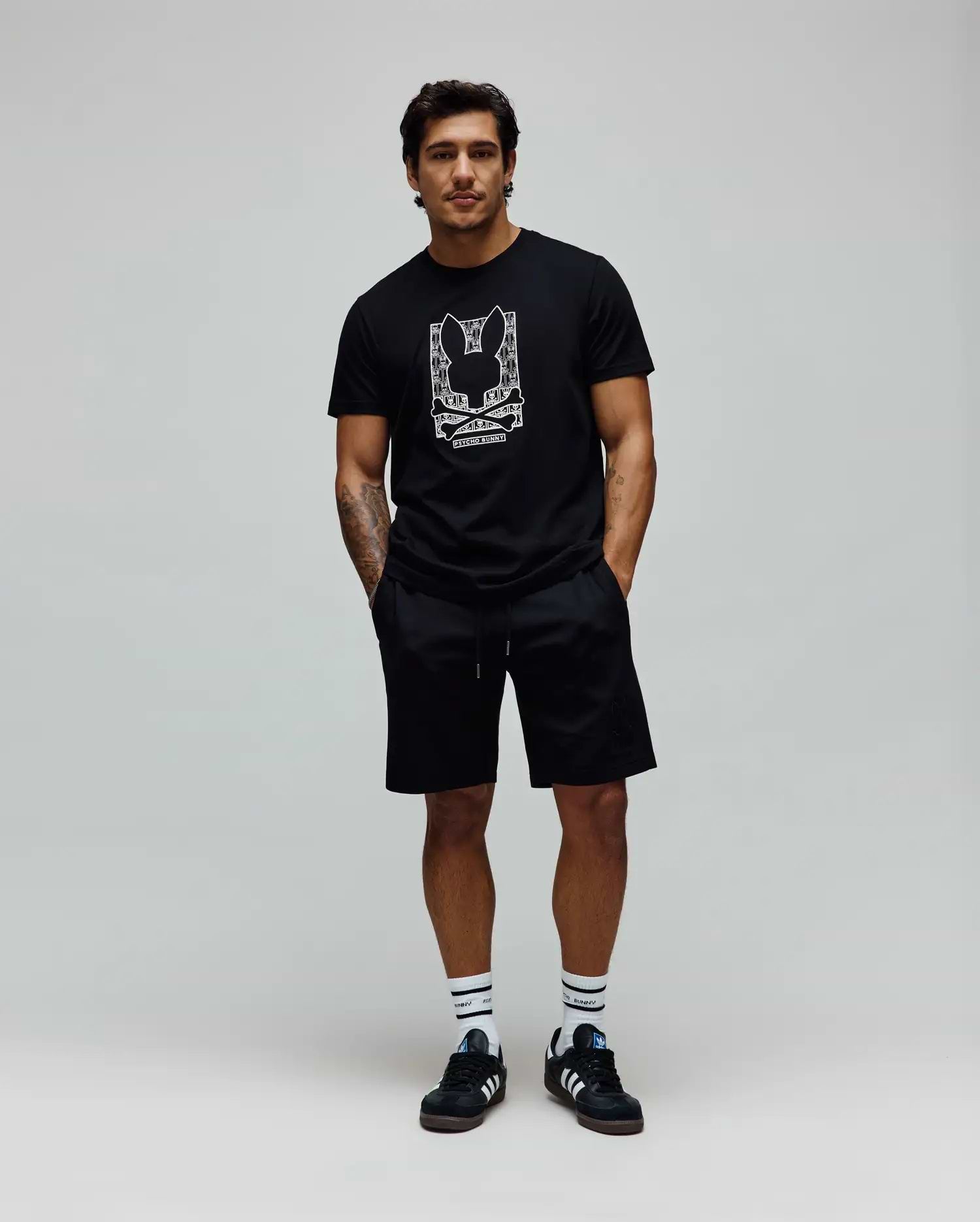 Mens Keon Embroidered Graphic Tee. Black classic-fit jersey t-shirt with a large white embroidered Psycho Bunny skull logo graphic and text on the chest, complemented by black relaxed shorts. (3)