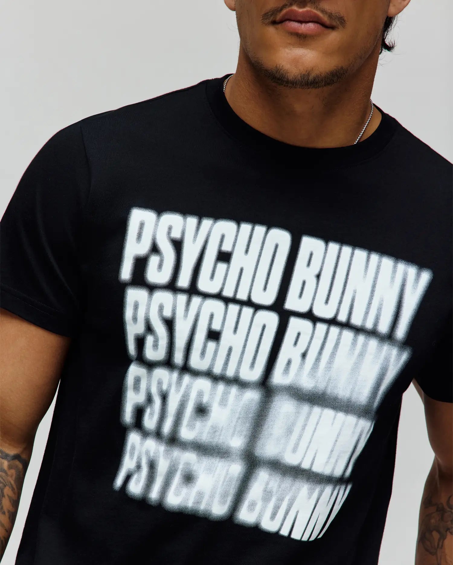 Mens Lawrence Graphic Tee, black classic fit jersey knit t-shirt featuring a large, central white blurred repeating PSYCHO BUNNY text graphic print. (3)