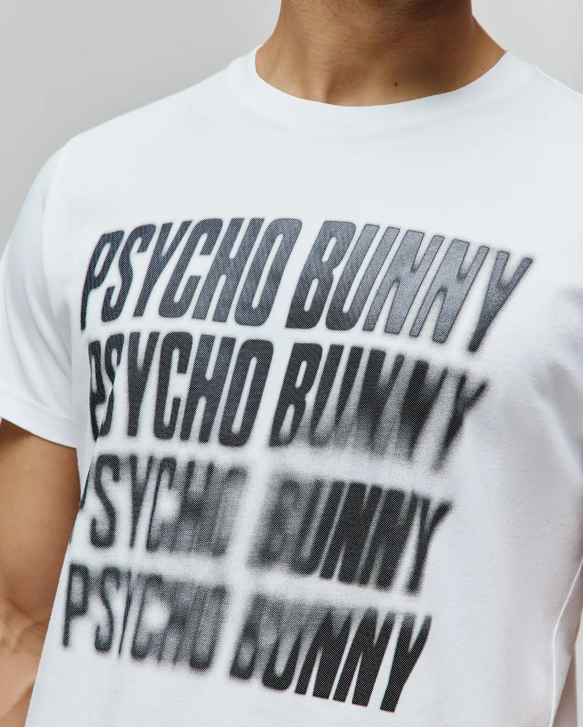Mens Lawrence Graphic Tee, a white classic fit jersey knit t-shirt featuring a large, central black and grey blurred Psycho Bunny text graphic with a subtle dot pattern. (3)