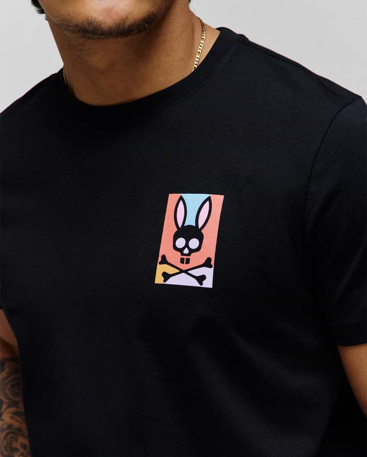 Black classic fit jersey t-shirt with a small, colorful Psycho Bunny skull graphic on the left chest, featuring pink, blue, orange, yellow, and purple accents. Mens Raphael Back Graphic Tee. (3)
