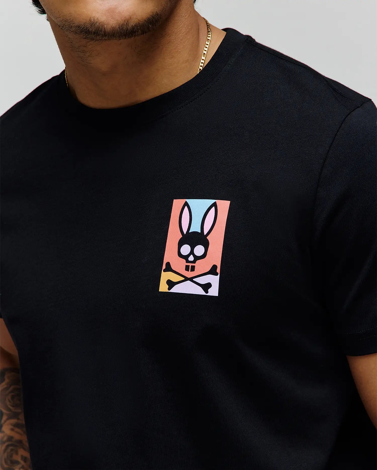 Black classic fit jersey t-shirt with a small, colorful Psycho Bunny skull graphic on the left chest, featuring pink, blue, orange, yellow, and purple accents. Mens Raphael Back Graphic Tee. (3)