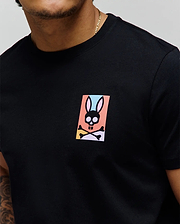 Black classic fit jersey t-shirt with a small, colorful Psycho Bunny skull graphic on the left chest, featuring pink, blue, orange, yellow, and purple accents. Mens Raphael Back Graphic Tee. (3)
