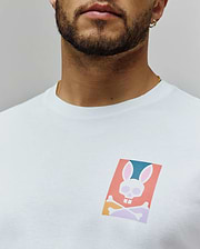 White Mens Raphael Back Graphic Tee, a classic fit jersey knit, featuring a small, vibrant chest graphic of the iconic Psycho Bunny skull logo in coral, teal, pink, and purple hues. (5)