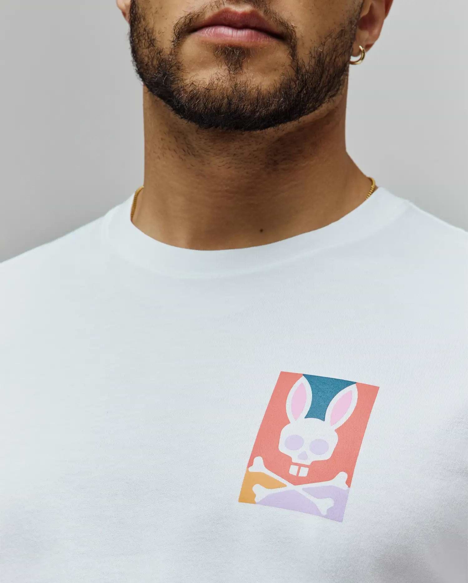 White Mens Raphael Back Graphic Tee, a classic fit jersey knit, featuring a small, vibrant chest graphic of the iconic Psycho Bunny skull logo in coral, teal, pink, and purple hues. (5)