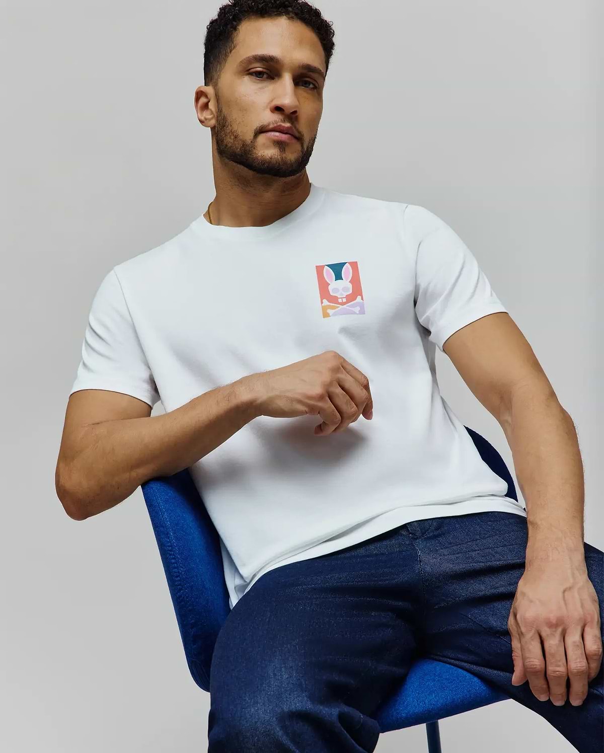 Mens Raphael Back Graphic Tee, a white classic fit jersey t-shirt featuring a small, vibrant Psycho Bunny skull and crossbones graphic on the left chest. (6)