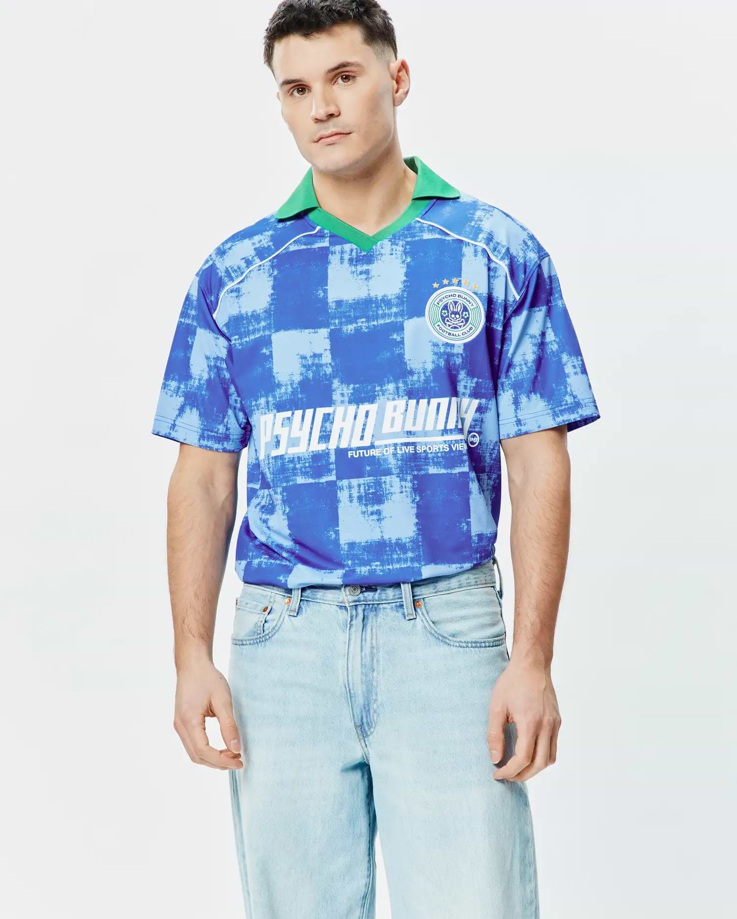 Mens Micah Oversized Soccer Jersey in blue and light blue distressed checkerboard pattern, featuring a green polo collar, white shoulder piping, a Psycho Bunny Football Club patch on the left chest, and large white Psycho Bunny text. (2)