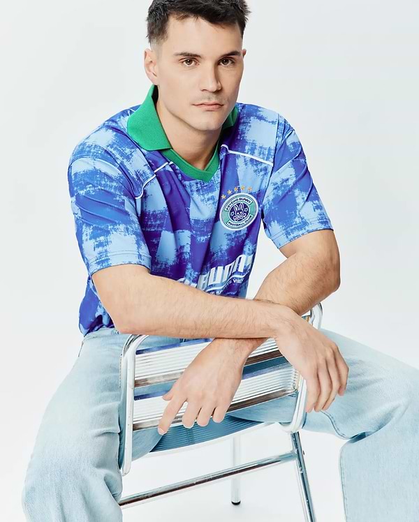 Mens Micah Oversized Soccer Jersey in blue abstract brushstroke pattern with a bright green collar, white shoulder piping, and a large circular Psycho Bunny Football Club emblem featuring the bunny skull and gold stars on the left chest. (4)