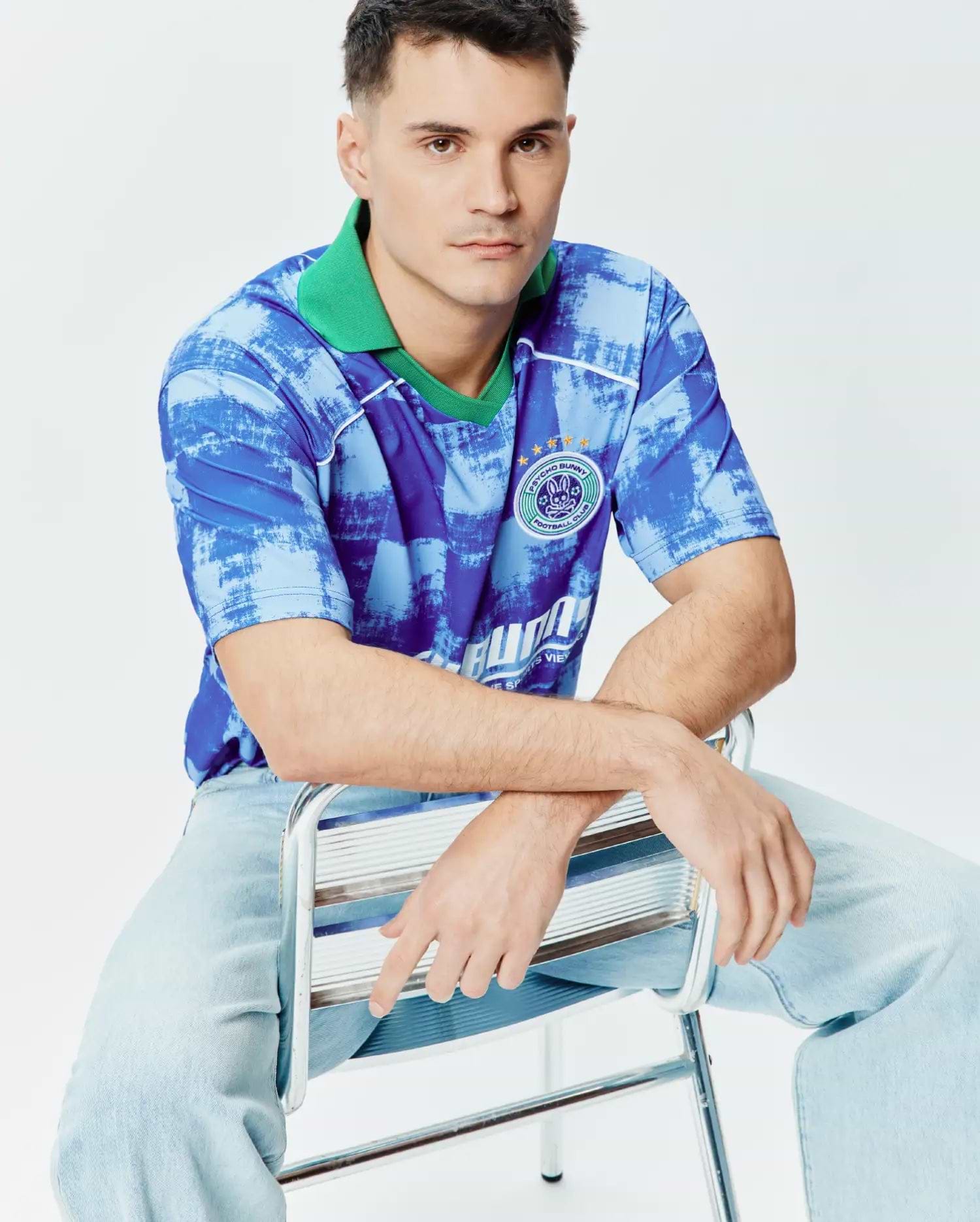 Mens Micah Oversized Soccer Jersey in blue abstract brushstroke pattern with a bright green collar, white shoulder piping, and a large circular Psycho Bunny Football Club emblem featuring the bunny skull and gold stars on the left chest. (4)