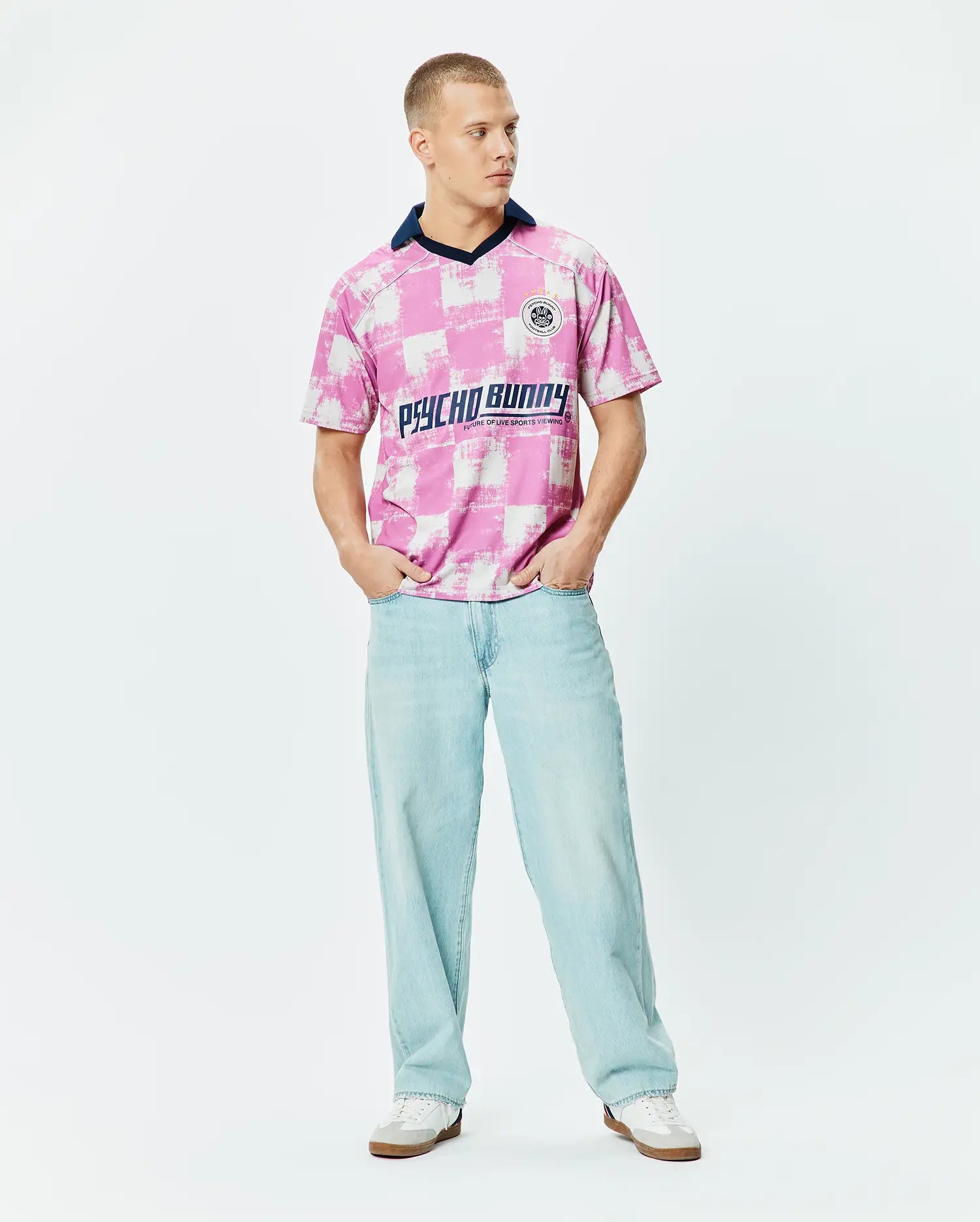 Micah Oversized Soccer Jersey in a bold pink and white distressed checkerboard pattern, featuring a navy V-neck collar, a small circular Psycho Bunny Football Club logo on the left chest, and a large Psycho Bunny text graphic across the chest. (4)