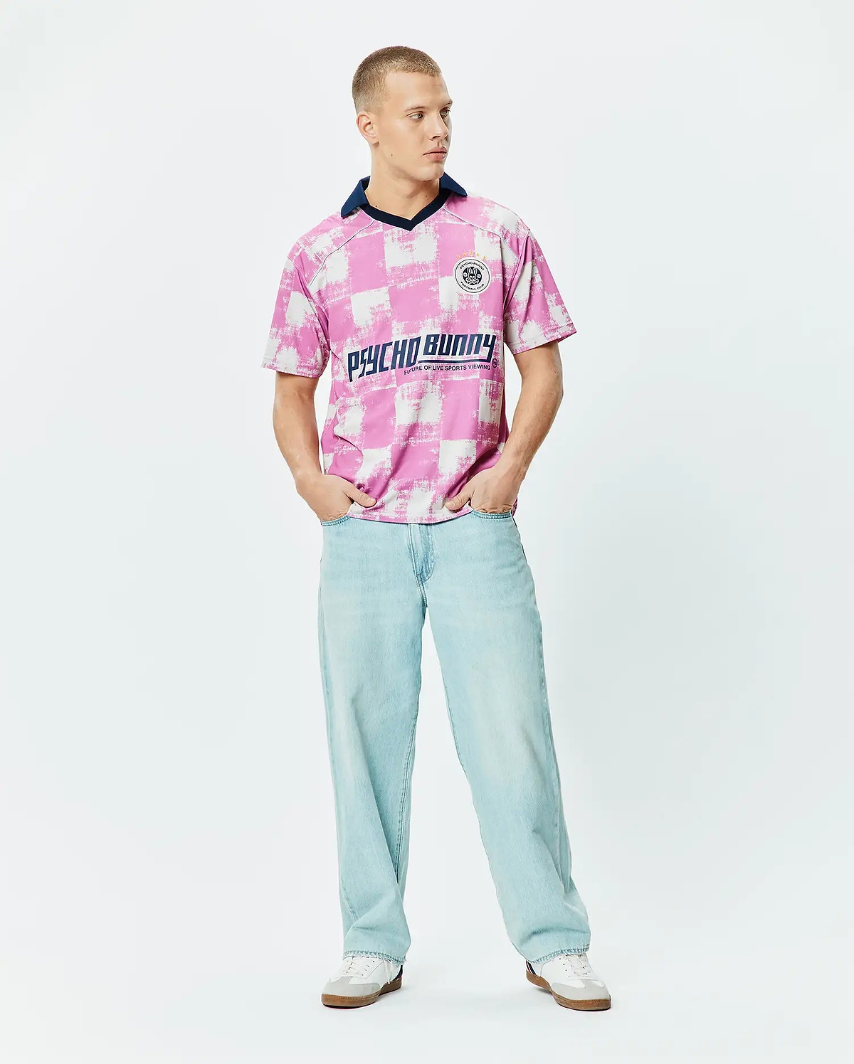 Micah Oversized Soccer Jersey in a bold pink and white distressed checkerboard pattern, featuring a navy V-neck collar, a small circular Psycho Bunny Football Club logo on the left chest, and a large Psycho Bunny text graphic across the chest. (4)