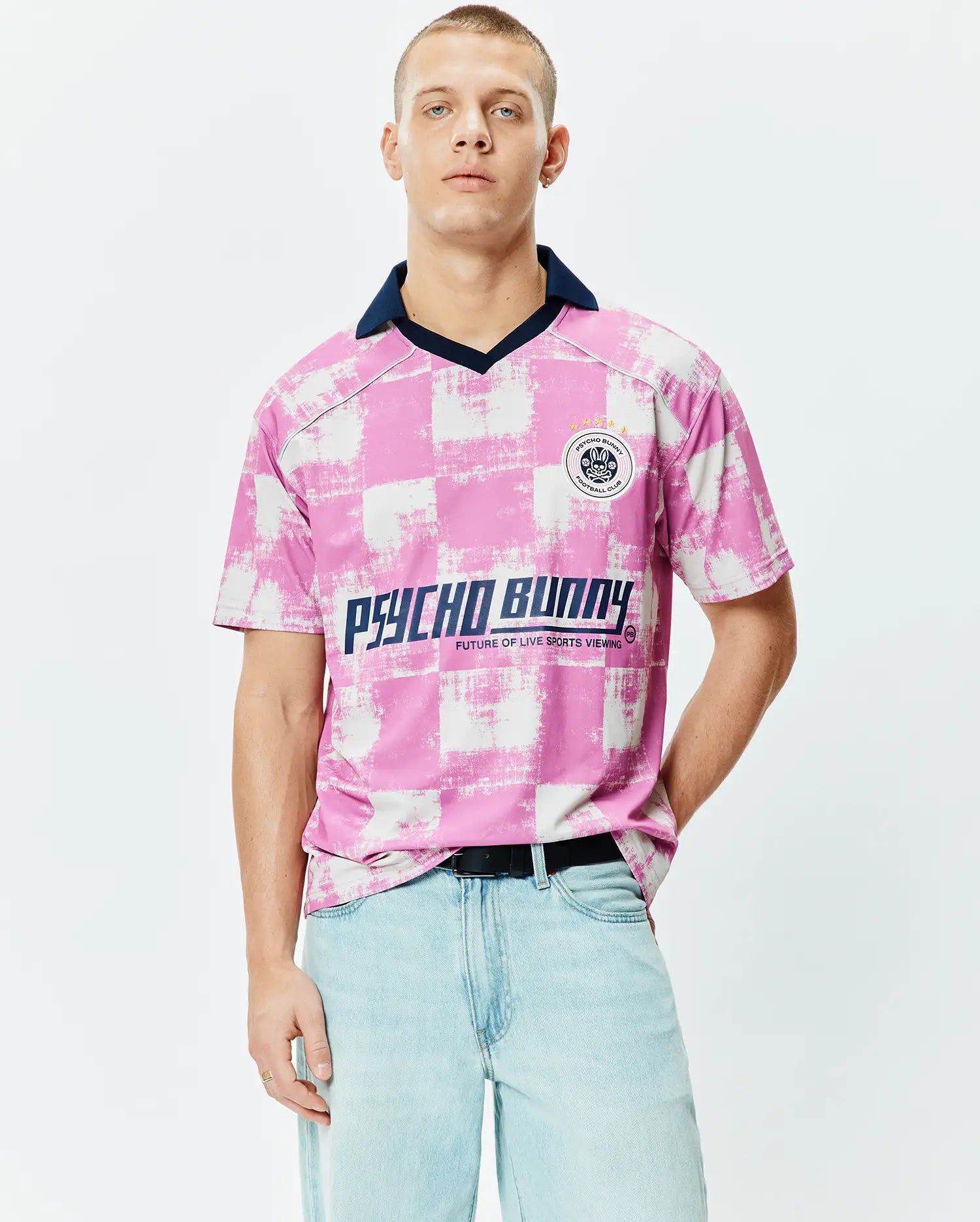 Micah Oversized Soccer Jersey in pink and white distressed checkerboard, with a navy collar, large Psycho Bunny chest text, and a circular Football Club patch featuring the iconic bunny skull logo. (1)