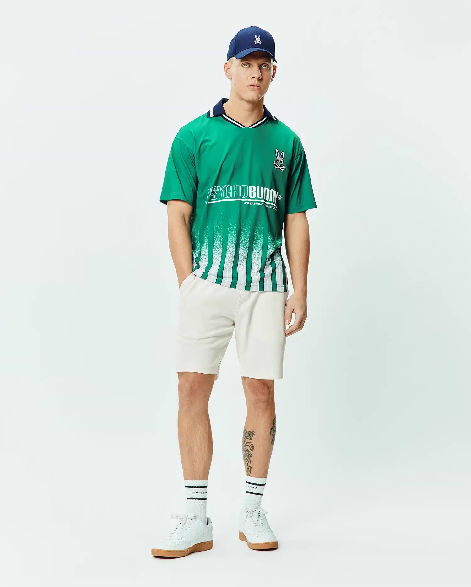 Mens Camden Oversized Soccer Jersey in vibrant green jersey fabric, featuring a navy collar, white fading vertical stripes, a large white PSYCHO BUNNY graphic, and a small embroidered bunny skull logo on the chest. (4)
