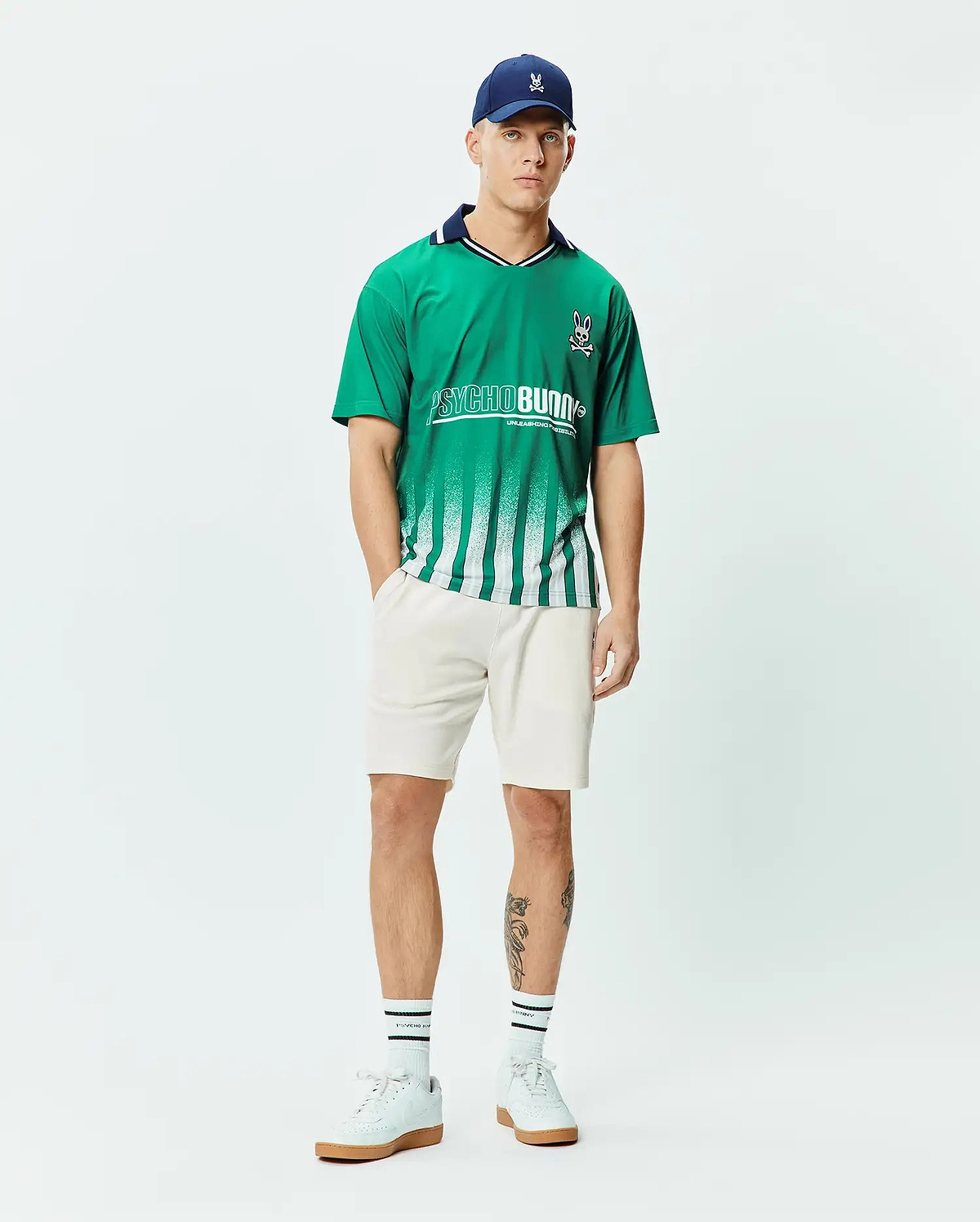 Mens Camden Oversized Soccer Jersey in vibrant green jersey fabric, featuring a navy collar, white fading vertical stripes, a large white PSYCHO BUNNY graphic, and a small embroidered bunny skull logo on the chest. (4)