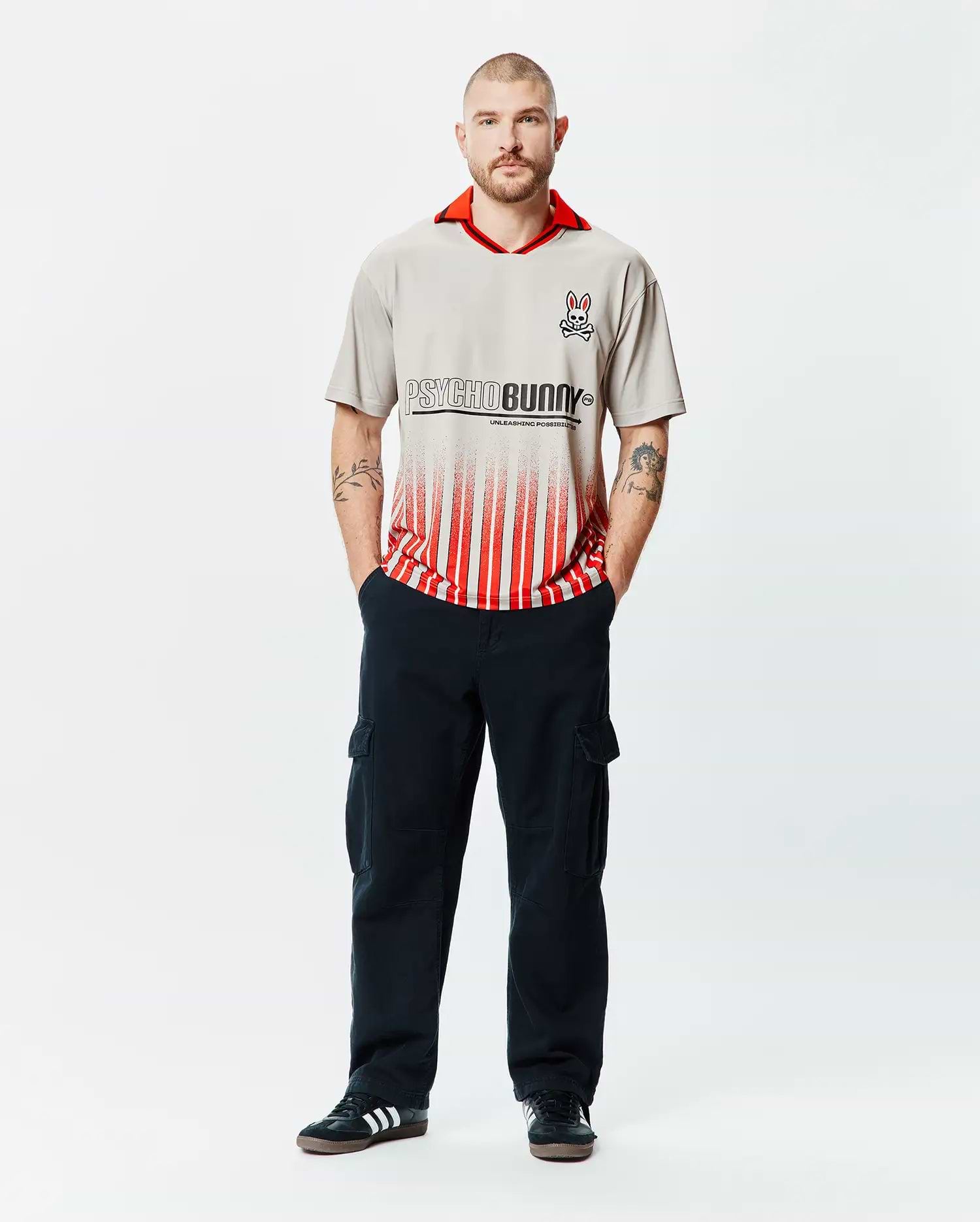 Mens Camden Oversized Soccer Jersey in stone grey with a vibrant red collar, featuring a large black Psycho Bunny text logo fading into bold red vertical stripes, and an embroidered bunny skull on the left chest. (4)