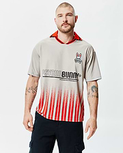 Mens Camden Oversized Soccer Jersey in light grey, featuring a red collar with black trim, an embroidered Psycho Bunny skull logo on the left chest, and a large PSYCHO BUNNY text graphic above red and white gradient stripes. (1)