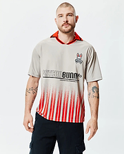 Mens Camden Oversized Soccer Jersey in light grey, featuring a red collar with black trim, an embroidered Psycho Bunny skull logo on the left chest, and a large PSYCHO BUNNY text graphic above red and white gradient stripes. (1)